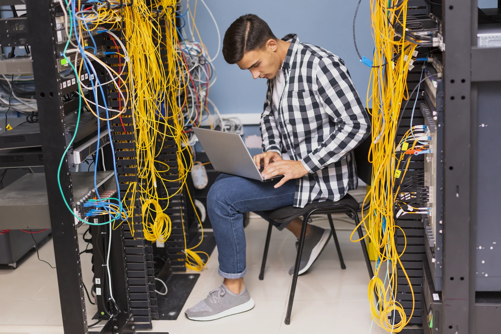 Técnico configurando un computador entre racks y cableado de comunicaciones